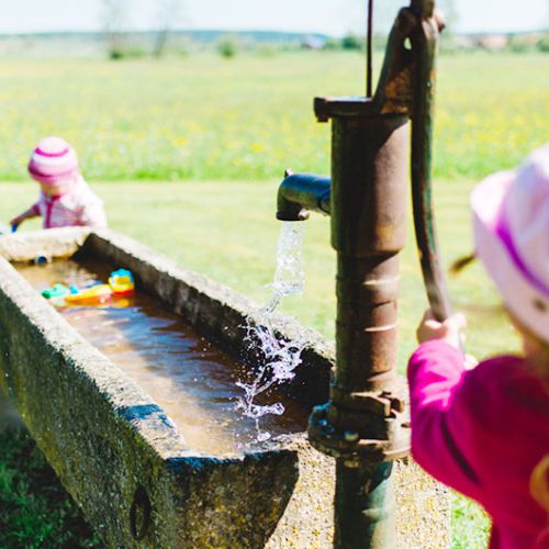 Zwei kleine Mädchen spielen mit einer Wasserpumpe